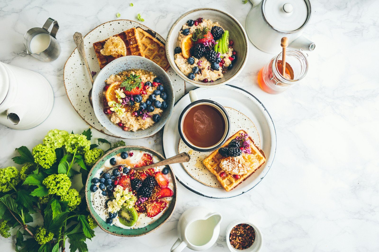 Breakfast table flatlay with porridge bowls, waffles, berries, tea and honey