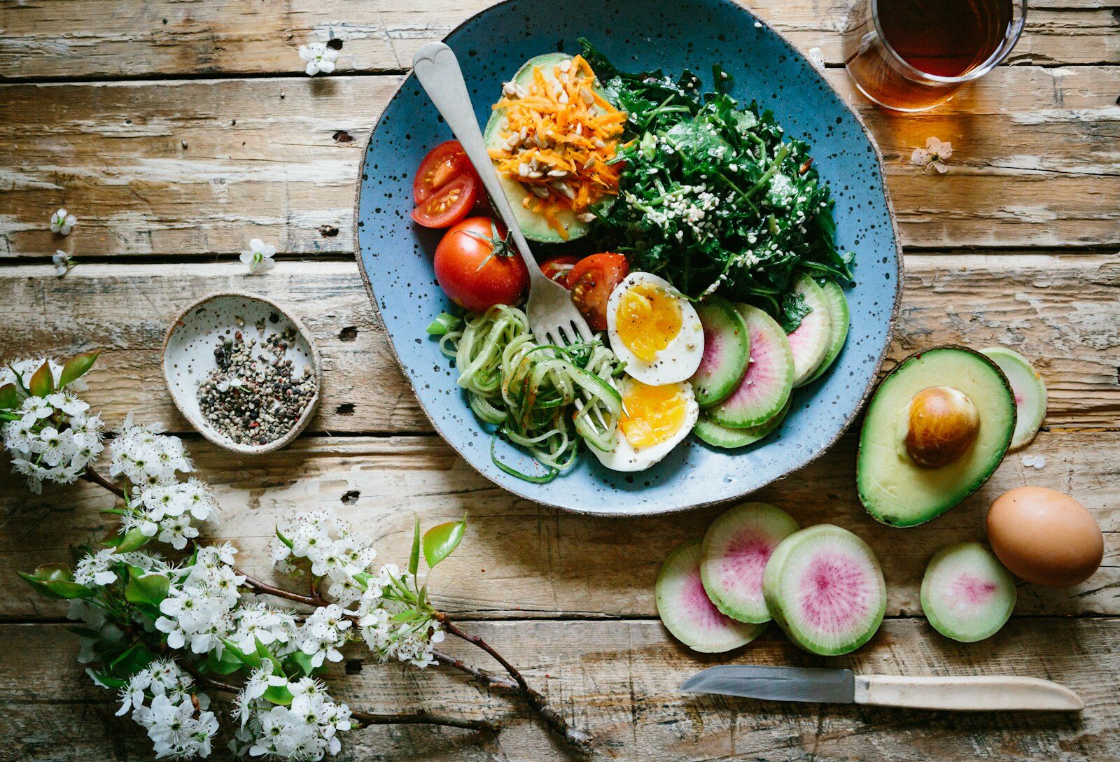 Healthy lunch bowl with egg, avocado, tomato and greens on a rustic wooden table