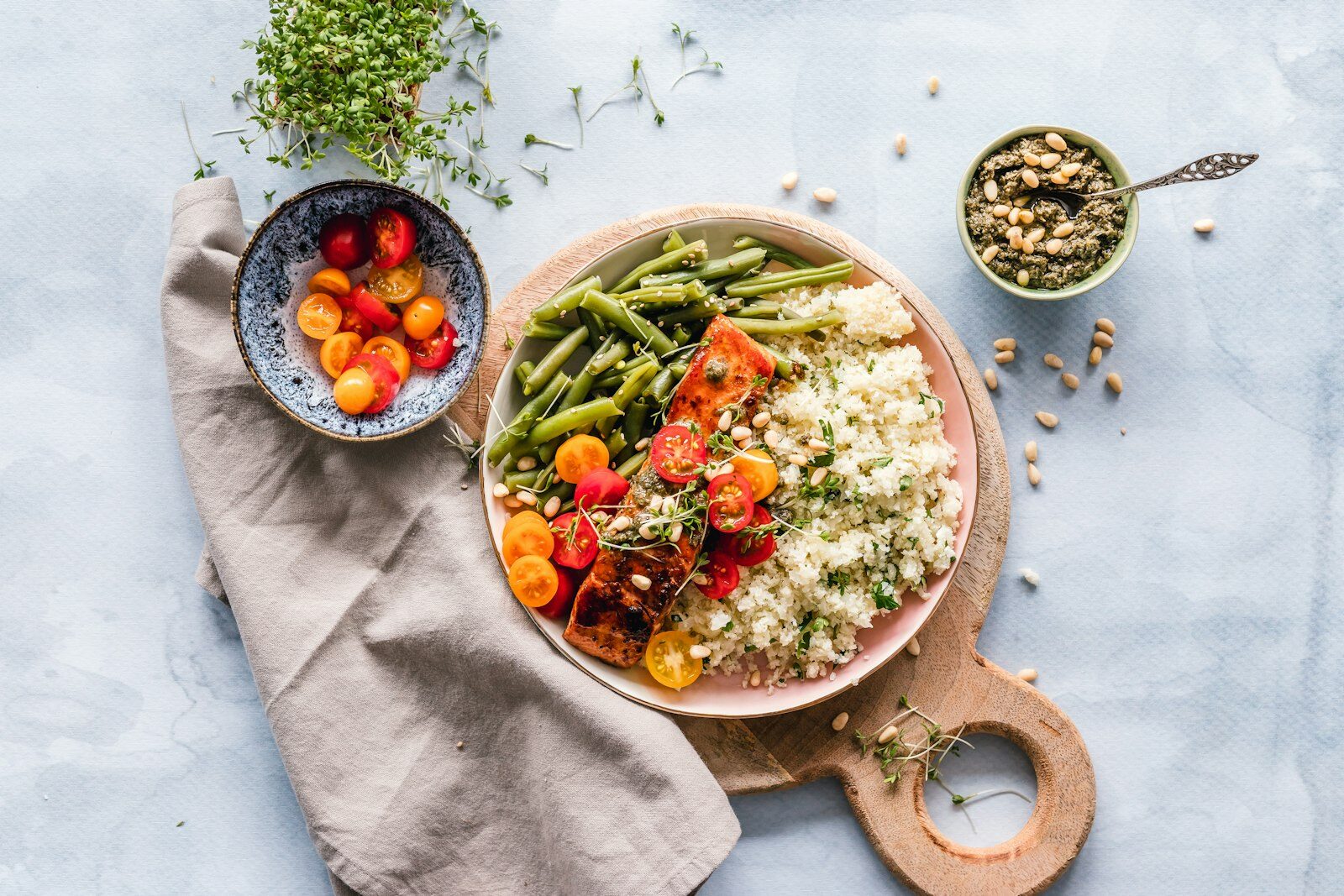 Overhead view of a portioned salmon dinner with green beans, grains, tomatoes and pesto