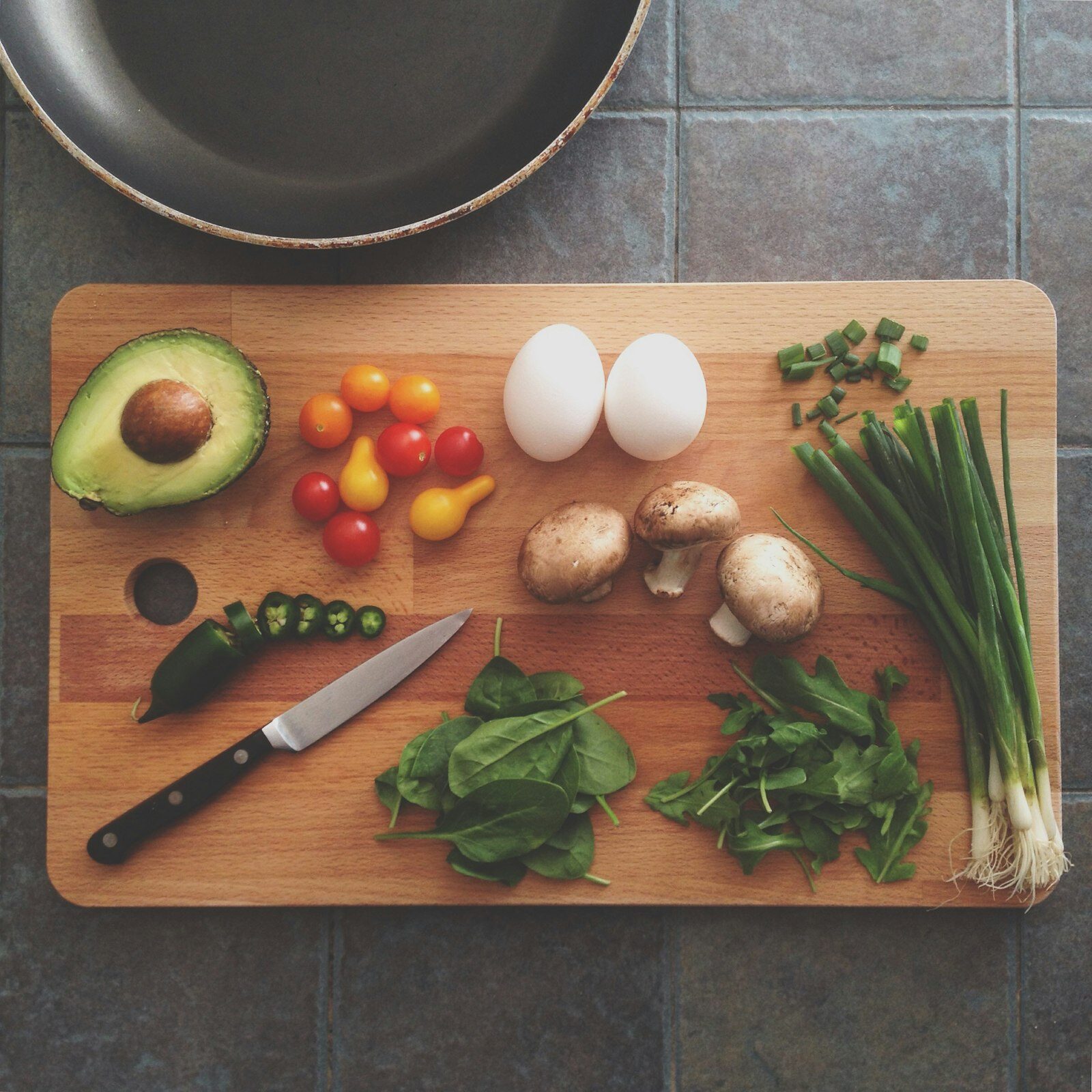 Fresh avocado, eggs, mushrooms, tomatoes and greens arranged on a wooden cutting board